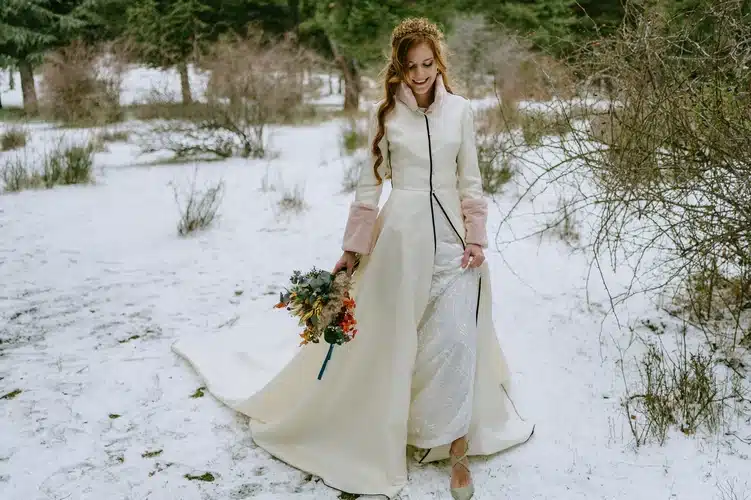 la novia acompañada de su Abrigo de Novia caminando sobre la nieve acompañada de su ramo